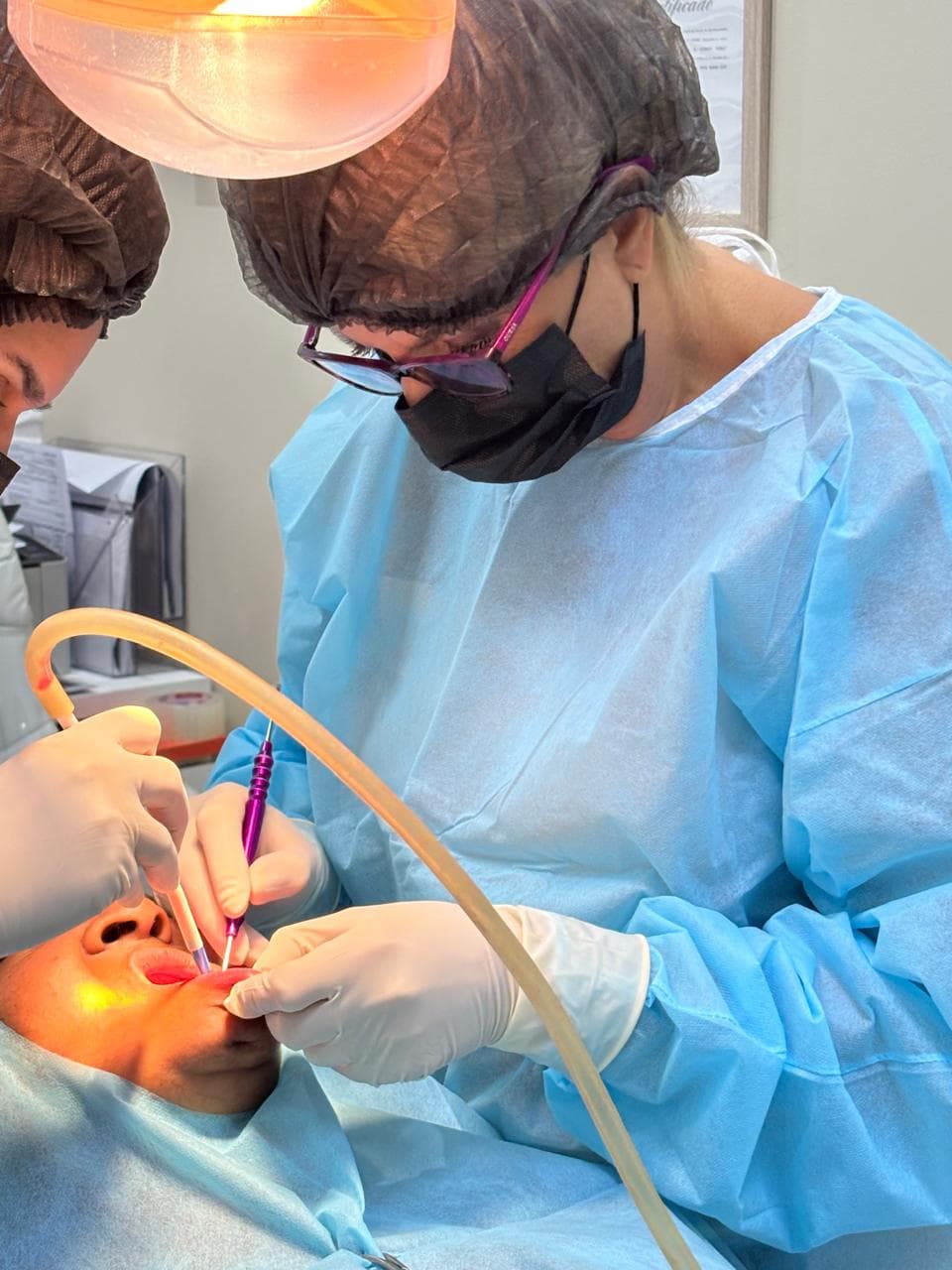 Dra. Michele Herreira realizando cirurgia odontológica com assistente no consultório em Suzano